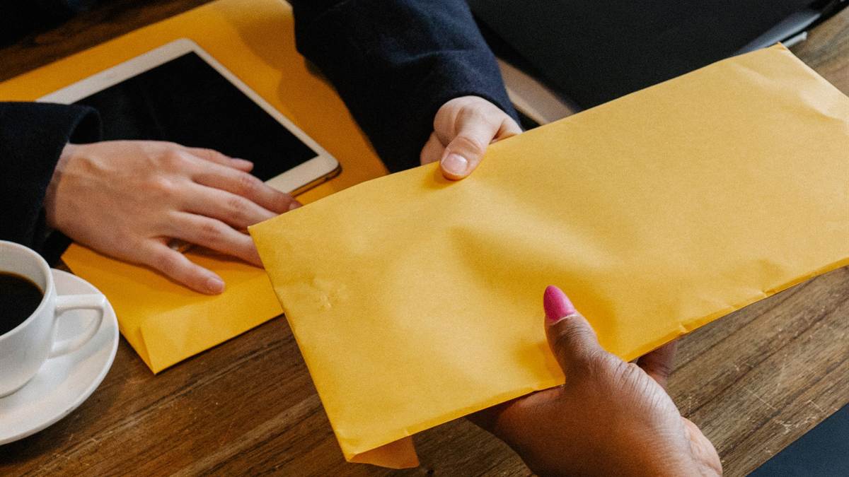 Two people passing a sealed document envelope across a table