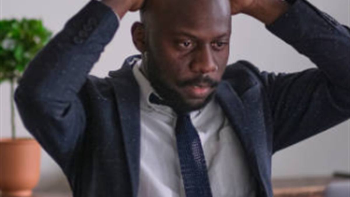 A person sitting back from a laptop with both hands on their head