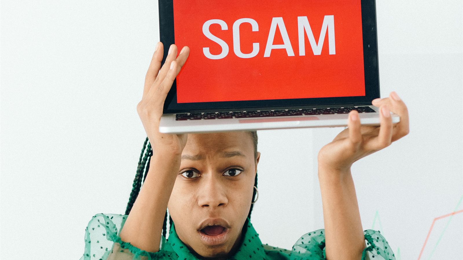 A person holding up a laptop displaying a full-screen scam warning